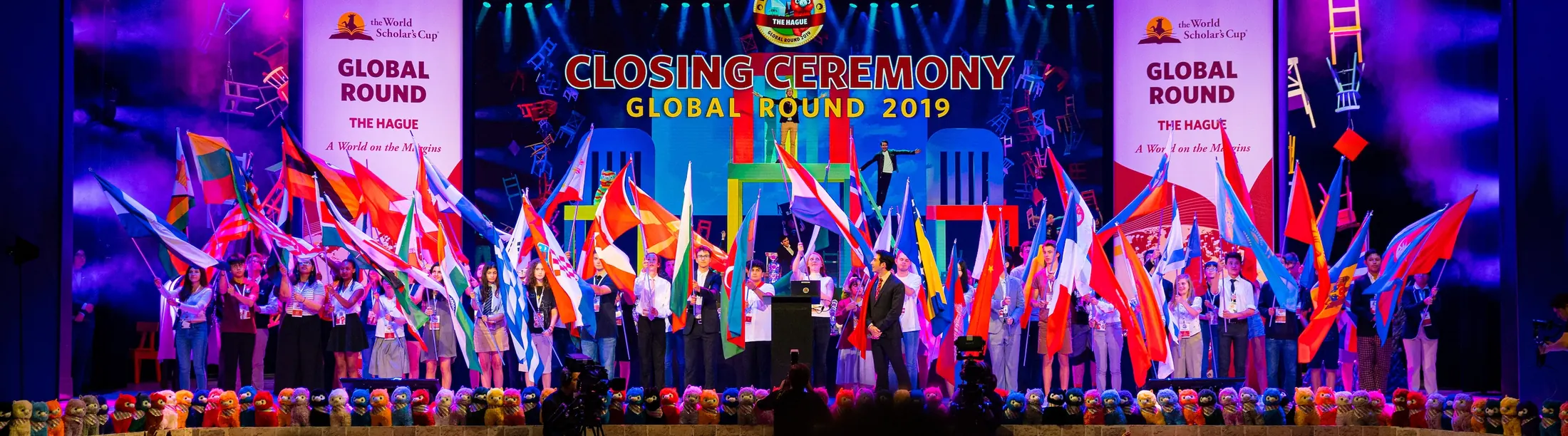 Scholars carry national flags across the stage at a closing ceremony